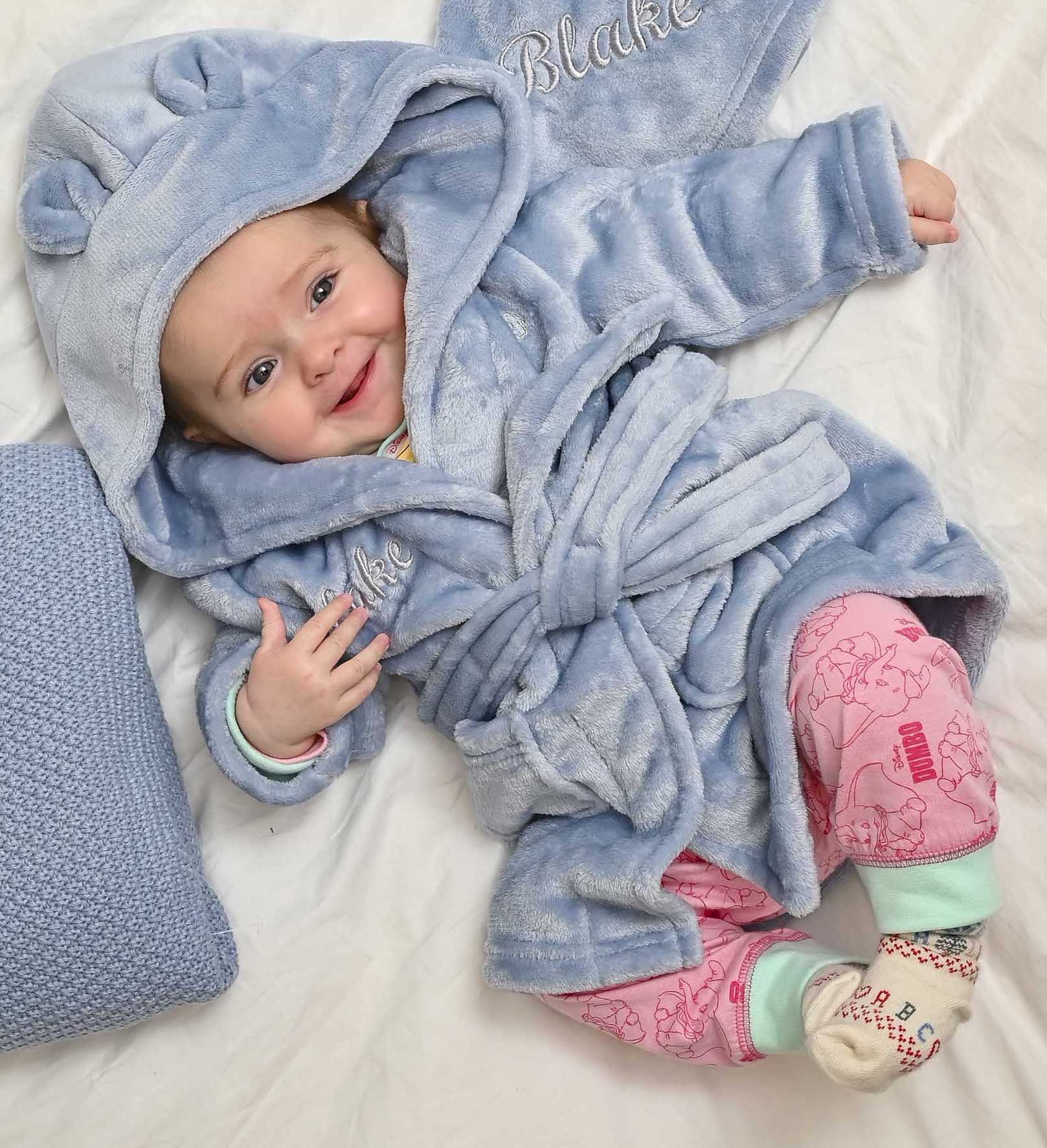  Babies personalised Dusky Blue hooded dressing gown. Made from super soft material, it features an elephant embroidery to the chest as well as detailing pom pom ears and a hood. Make it extra special by adding a personalised touch.