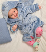  Babies personalised Dusky Blue hooded dressing gown. Made from super soft material, it features an elephant embroidery to the chest as well as detailing pom pom ears and a hood. Make it extra special by adding a personalised touch.